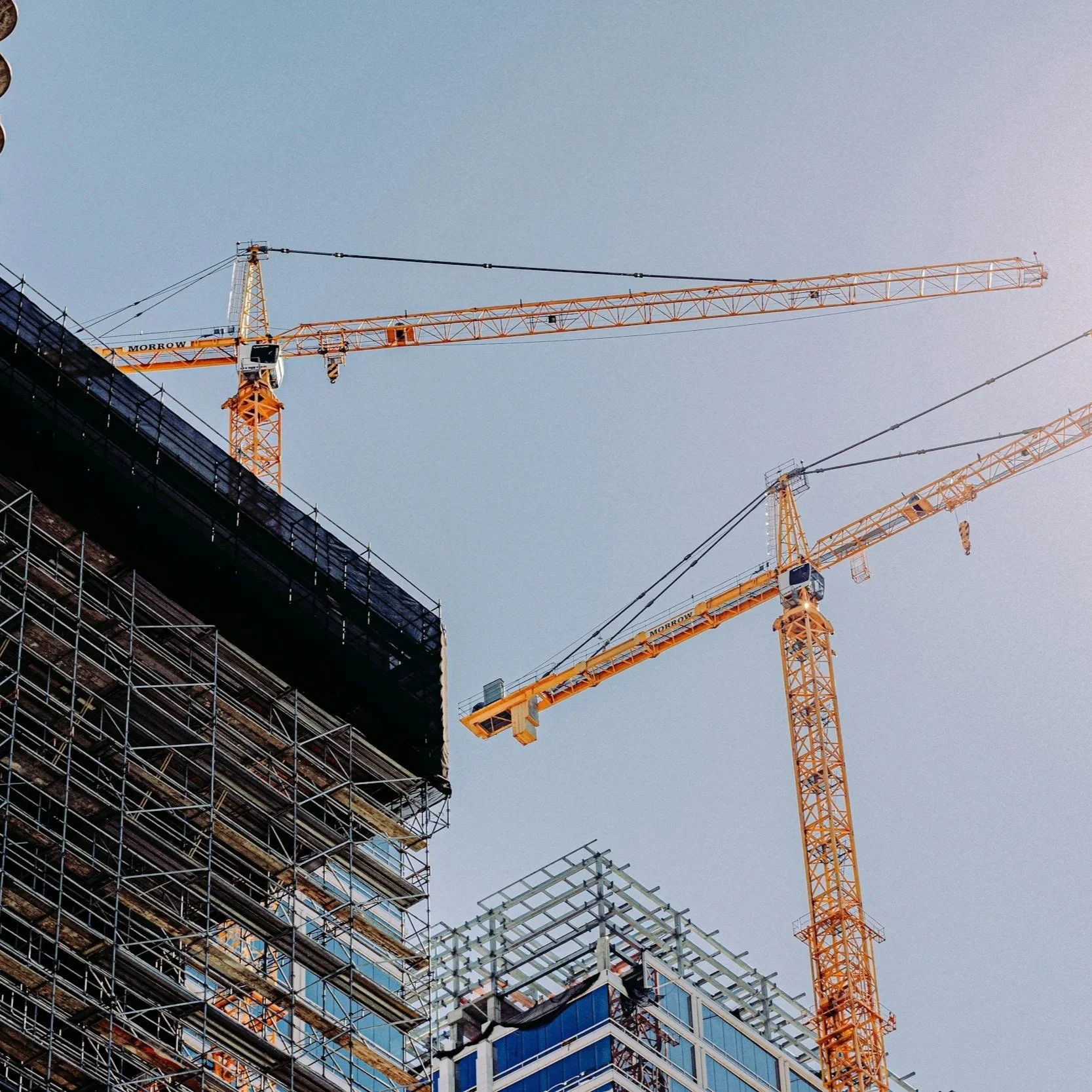 Construction site with several tall yellow cranes and partially built high-rise buildings.