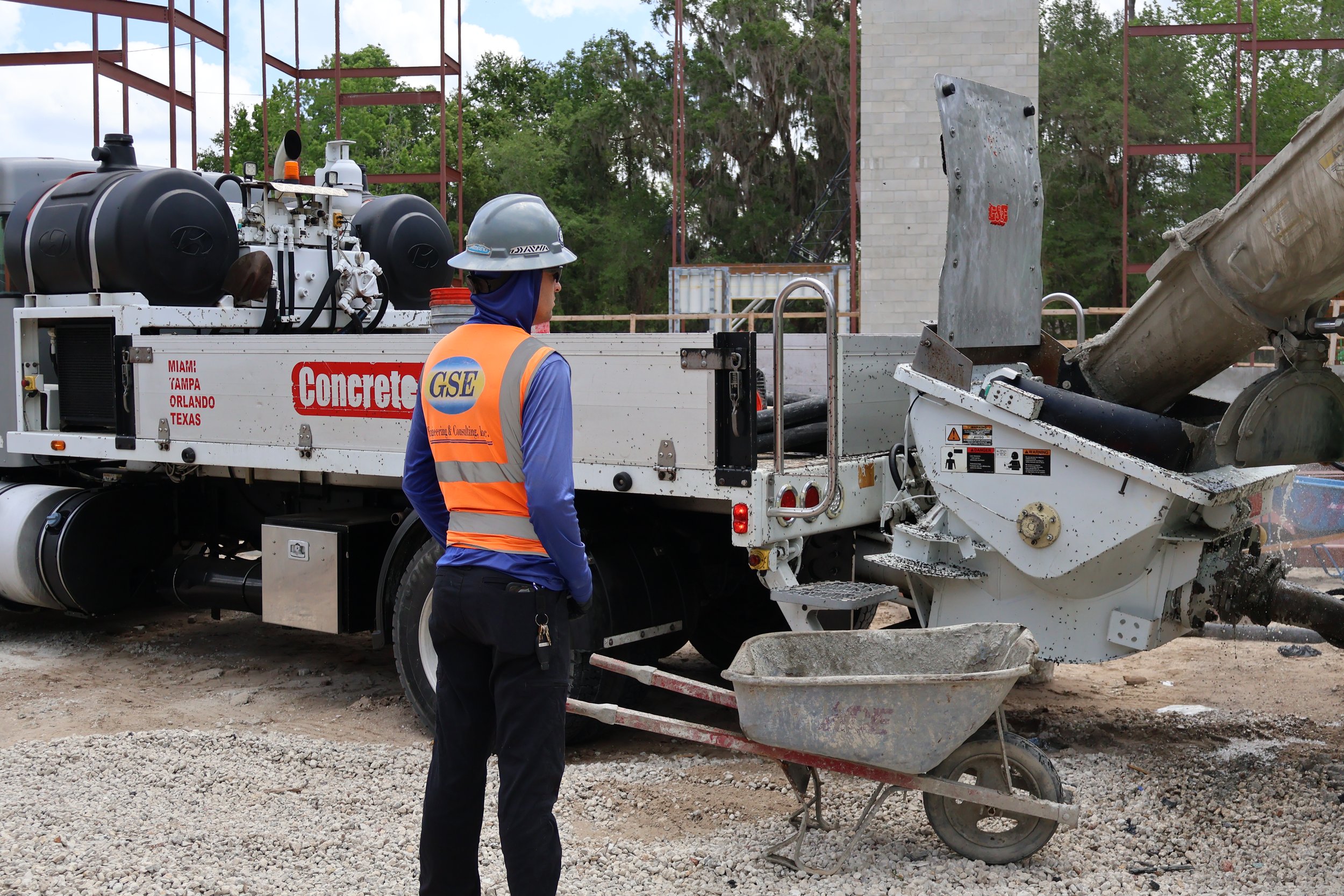 A construction worker standing in front of concrete pumping equipment at a construction site with trees in the background.