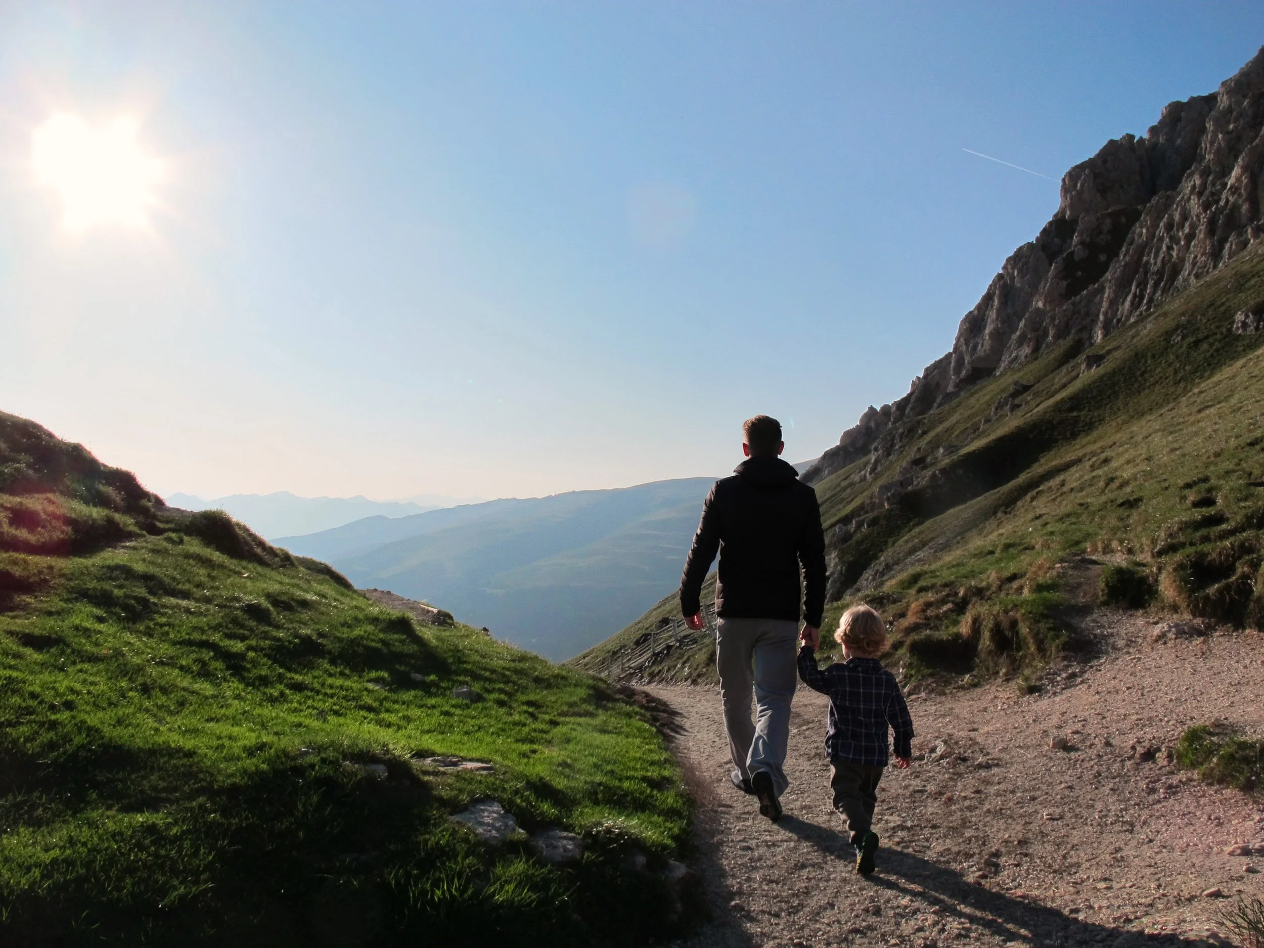321 Billingsly Ct, Ste 9 Franklin, TN 37067. Summit Neuropsychology, PLLC. A person and a child walk along a dirt trail through a mountainous landscape with green grassy slopes.
