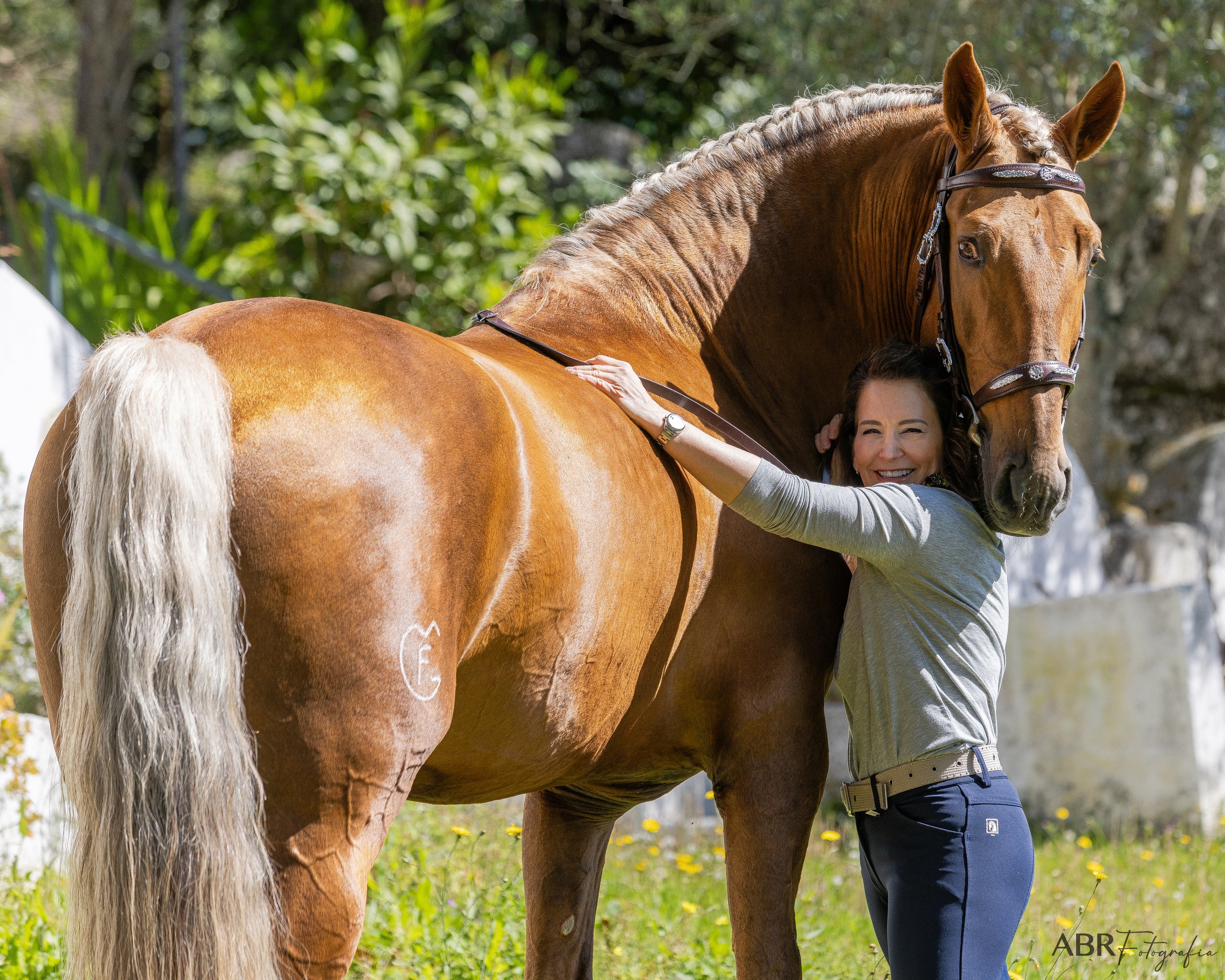 A woman hugging a chestnut horse outdoors with greenery in the background.