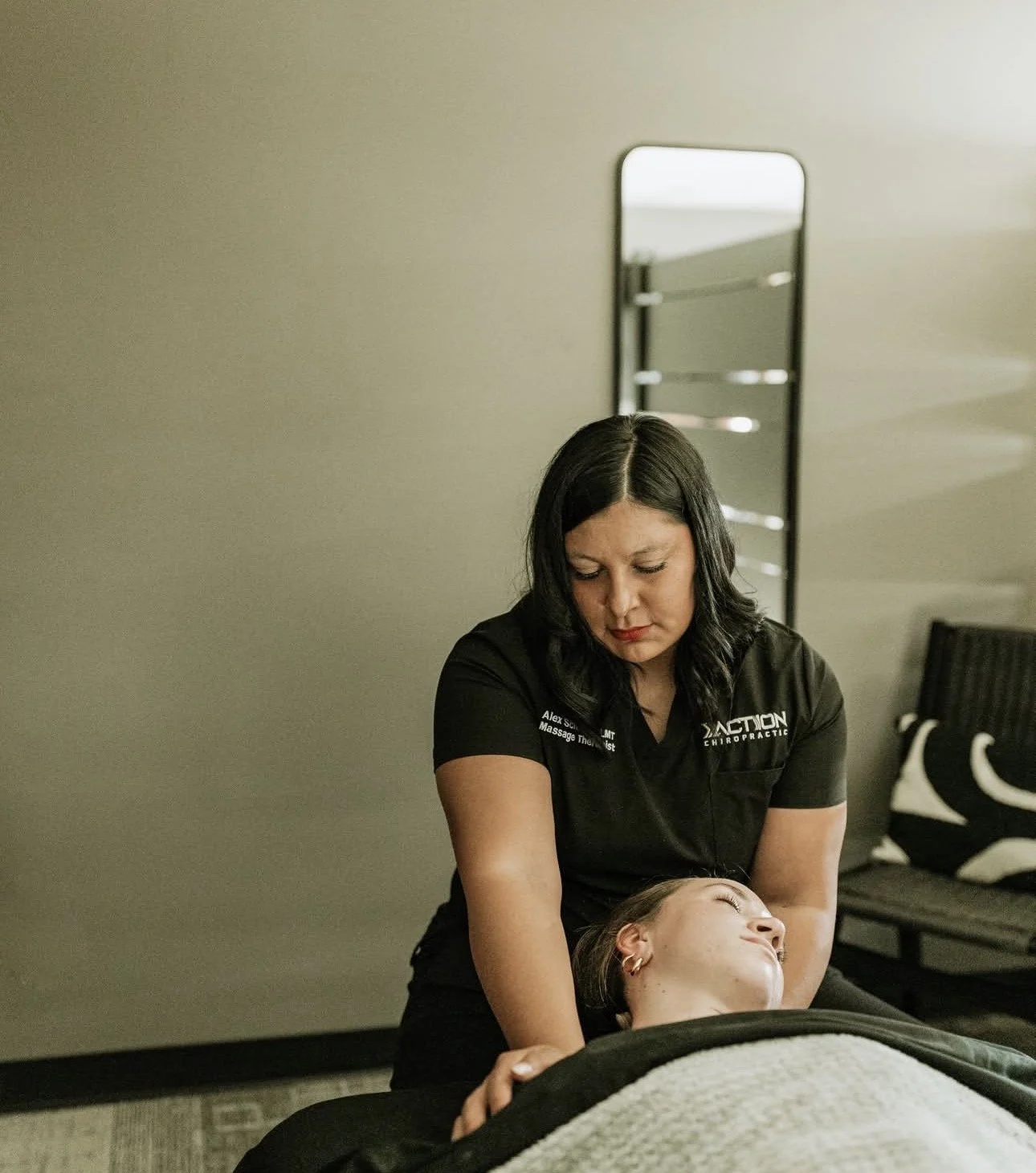 Chiropractic massage therapist performing a cervical adjustment on a patient lying face up on a treatment table.