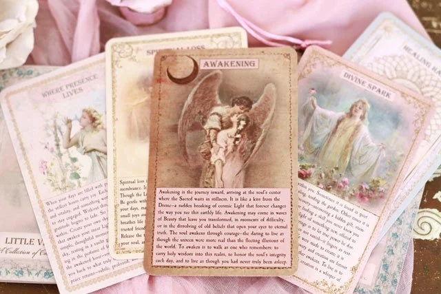 Collection of spiritual and angelic tarot or oracle cards, some featuring angels, divine messages, and mystical themes, arranged on a pink cloth.