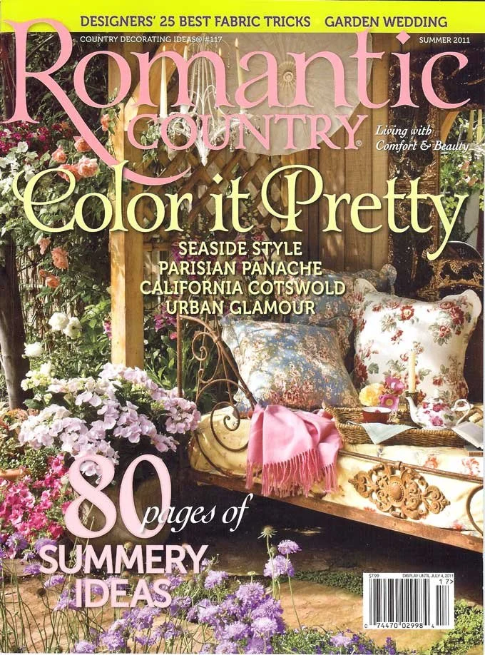 Magazine cover titled 'Romantic Country' with a garden scene featuring a vintage-style bench with floral cushions, surrounded by pink, purple, and white flowers, and a pink throw blanket draped over the bench.