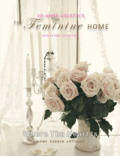 A bouquet of pale pink roses in a white vase on a white table, with white candles and ornate candle holders in the background, and sheer curtains allowing soft light into the room.