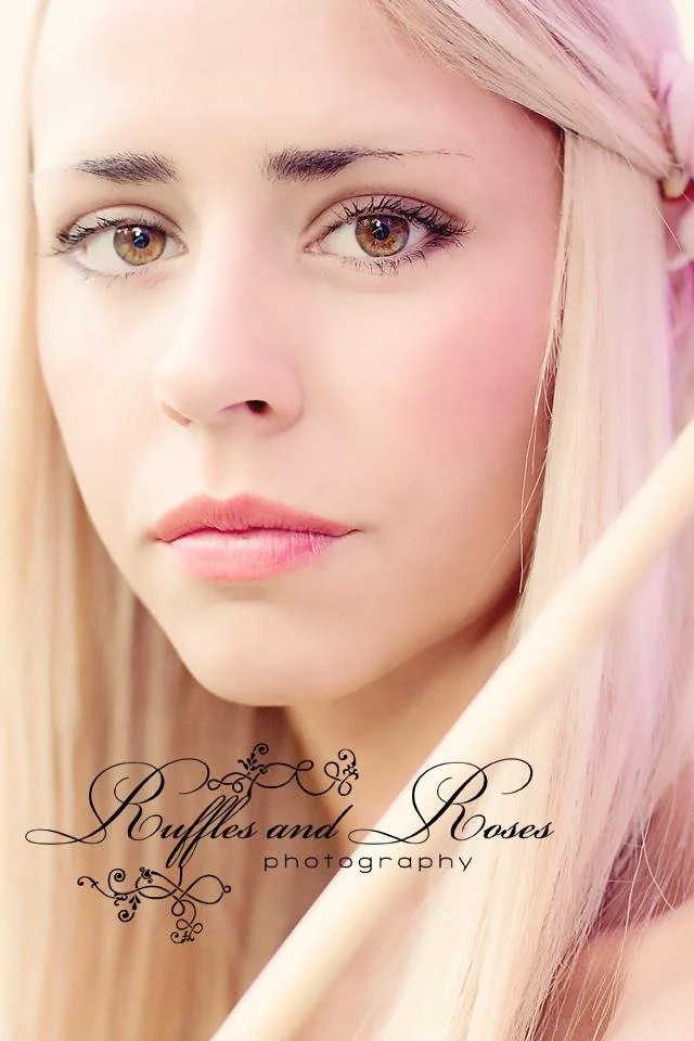 Close-up of a young woman with long blonde hair, fair skin, and hazel eyes looking into the camera with a neutral expression.