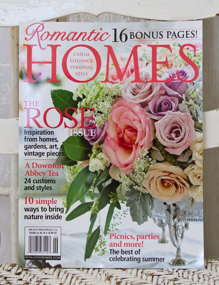 Cover of Romantic Homes magazine featuring a bouquet of pink, purple, and white roses with greenery, on a table with a silver bowl, and text about home decor, gardens, and summer celebrations.