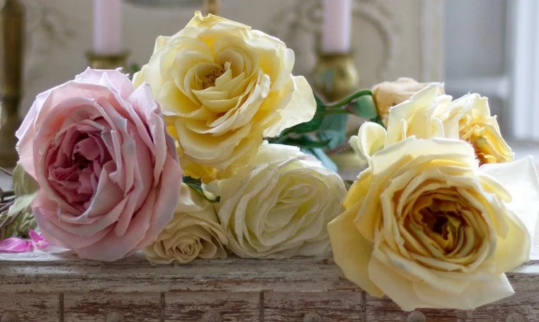 A bouquet of pale pink, yellow, and cream roses on a rustic wooden surface.