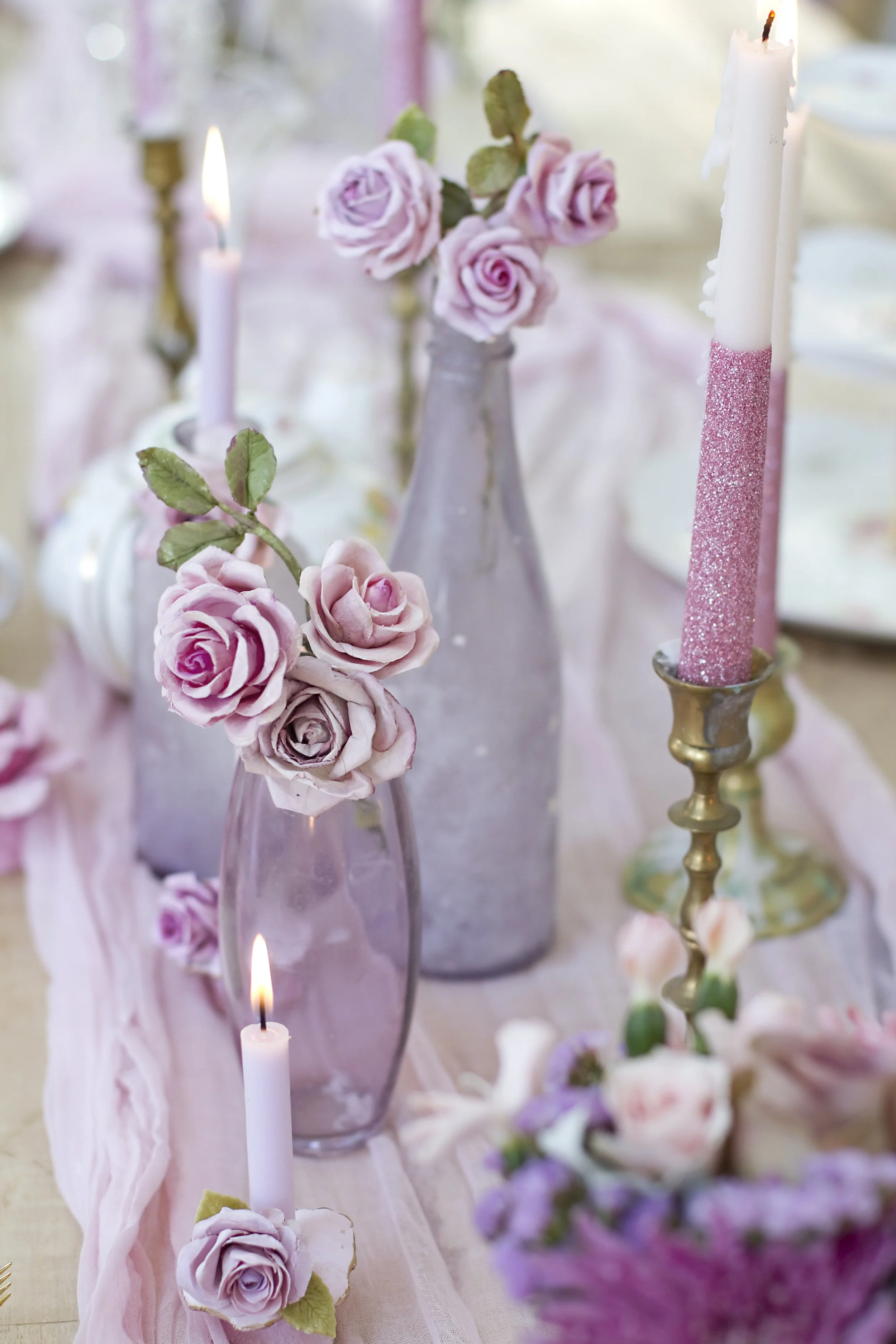 A table decorated with pink roses in vases and pink candles, with additional flowers in the background.