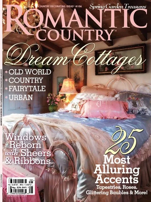 Cover of Romantic Country magazine featuring a cozy bedroom with a large bed, pink and white linens, a bedside lamp, a pink flower arrangement, and rustic wooden ceiling beams.