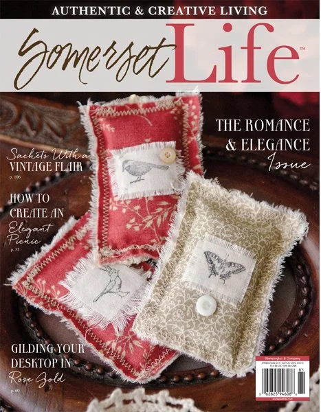 Cover of Somerset Life magazine featuring a close-up of decorative fabric sachets with vintage-style bird embroidery, placed on a wooden surface.