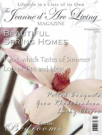 Close-up of a magazine cover titled 'Jeanne d’s Are Living' featuring a large flower with soft pink and cream petals and a red center, with text about beautiful spring homes, summer food, tips, and bedroom ideas.