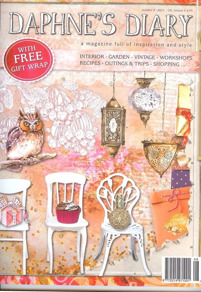 Cover of Daphne's Diary magazine featuring a pink and orange watercolor background, decorative lanterns hanging, illustrated branches with berries, and decorated chairs with gifts, candles, and a cupcake, with headlines about inspiration, style, and 