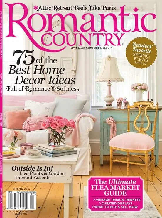 The cover of Romantic Country magazine featuring a pastel-colored living room with a white sofa, pink flowers, a blue side table, and a pink chair. The magazine highlights home decor ideas, outdoor plants, and flea market buying tips.