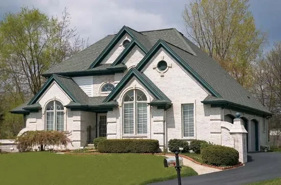 A large modern house with white brick, green-trimmed gables, and arched windows. The neat lawn and trimmed hedges add a welcoming feel.