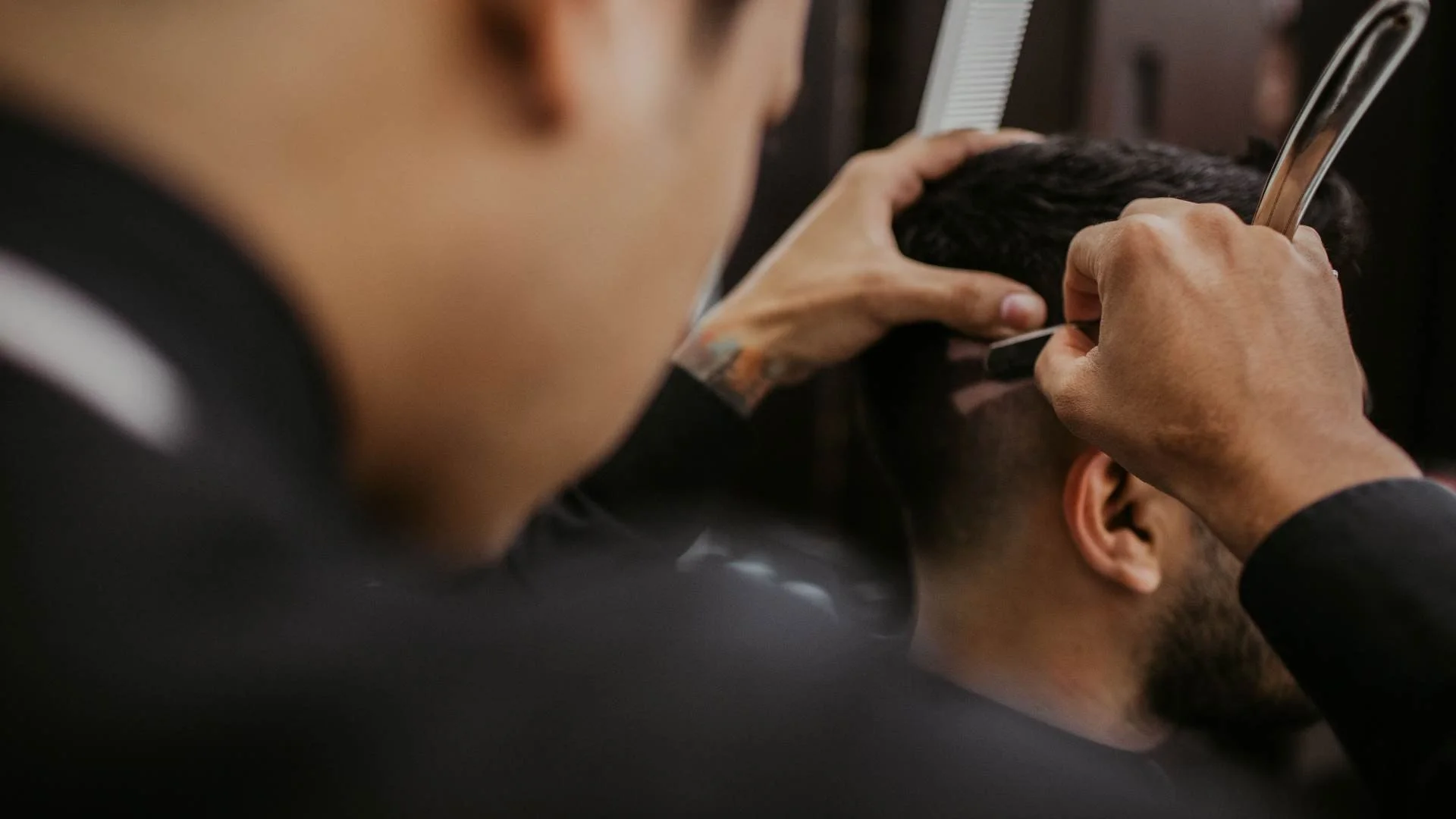 Barber cutting a man's hair with clippers in a barbershop.