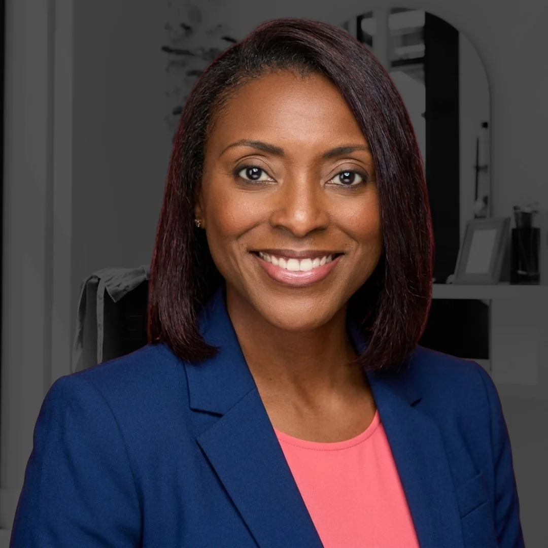 Professional woman with a friendly smile, wearing a blue blazer and pink top, in an office setting.