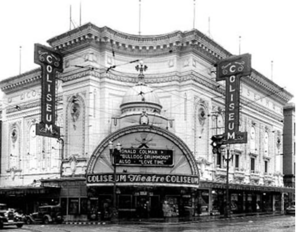 Black and white photo of the historic Coliseum Theatre building, with signs reading "Coliseum Museum" on the sides and above the entrance, and a marquee advertising a show featuring Ronald Colman and Bulldog Drummond.