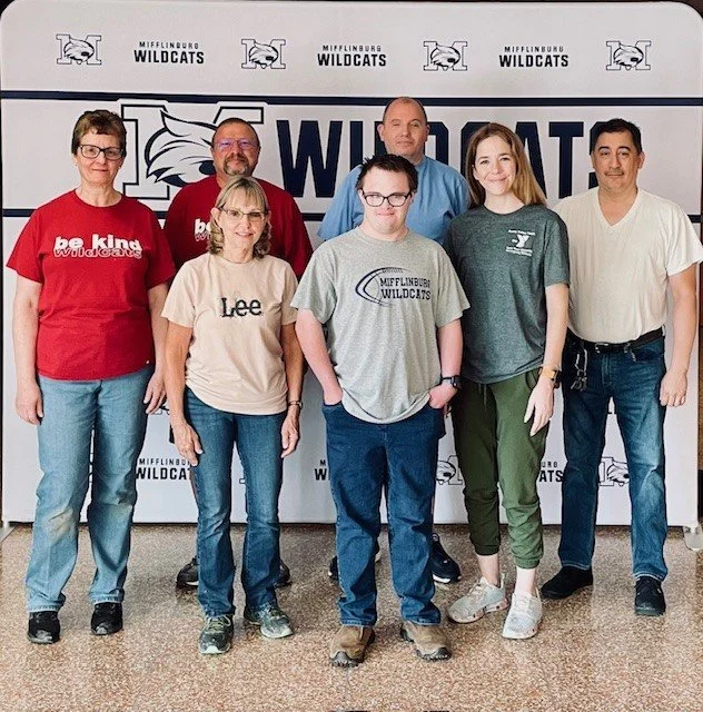 Seven people standing in front of a Mifflinburg Wildcats banner.