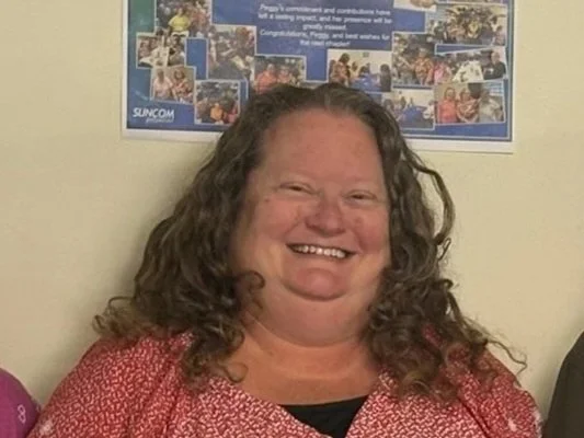 A woman with curly hair smiling in front of a bulletin board with photos.