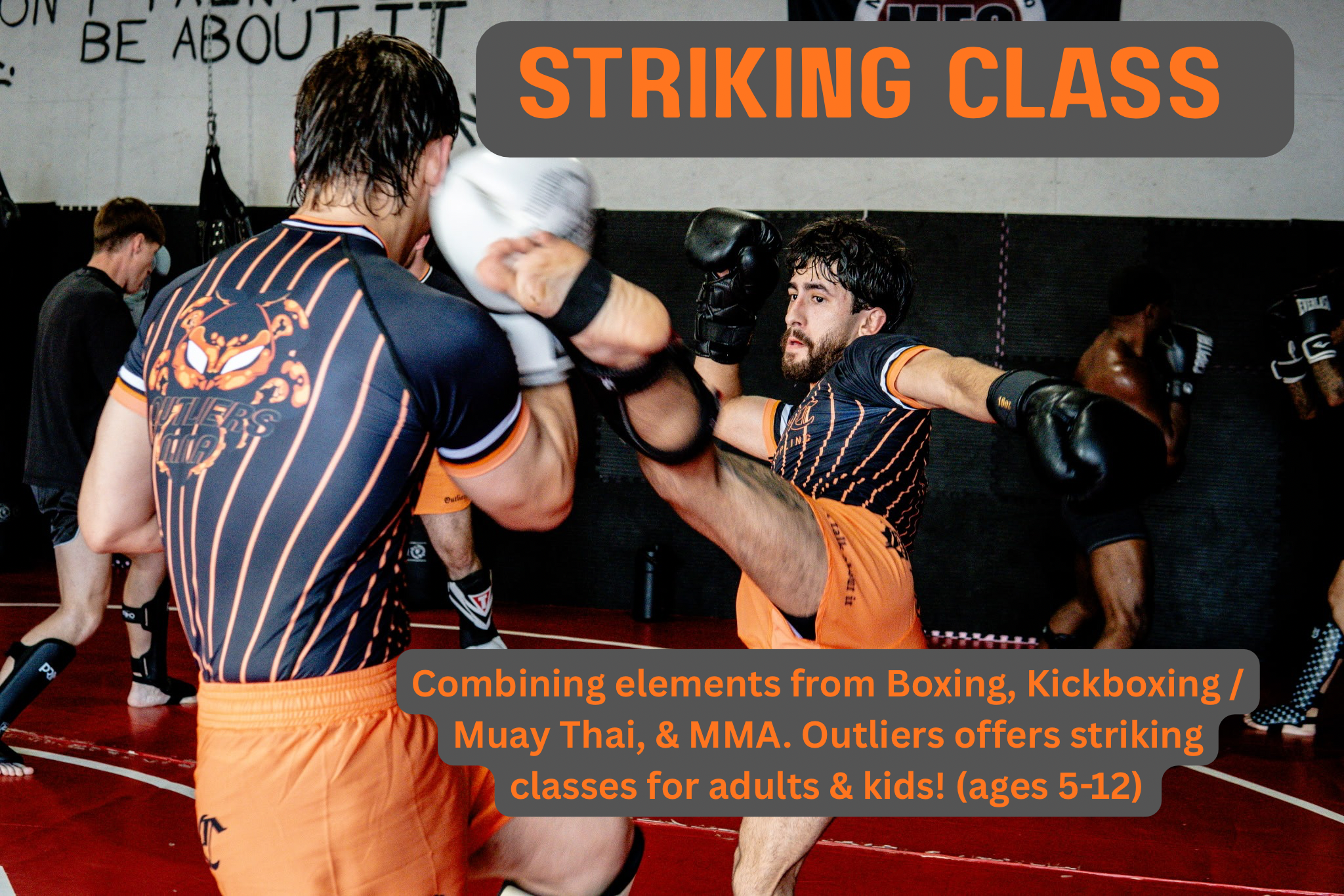 Two men in sports attire practicing boxing and kickboxing techniques during a training session at an indoor gym. other pairs of people training in the background. The gym has a wall with motivational text.