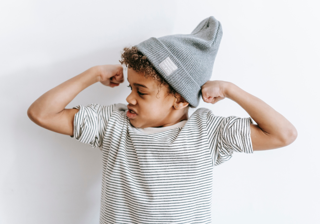 young boy in a beanie hat flexing his arms to show his muscles