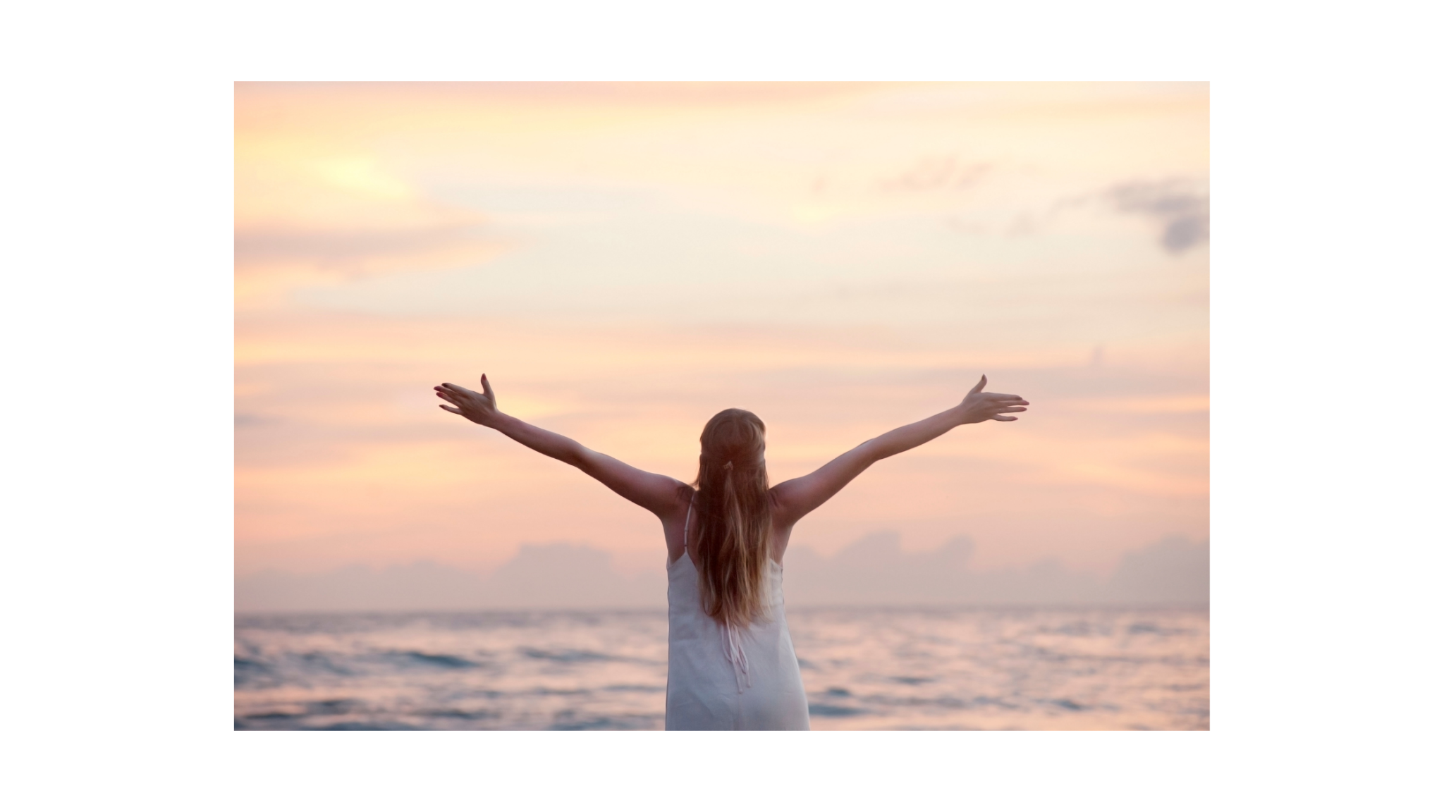 woman in front of sunset on the ocean with arms in the air
