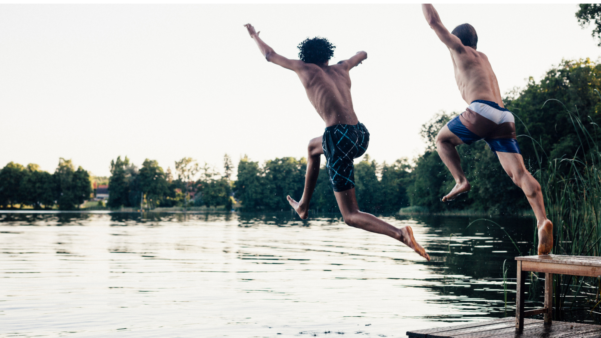 two teenage boys jumping off of a dock into a lake