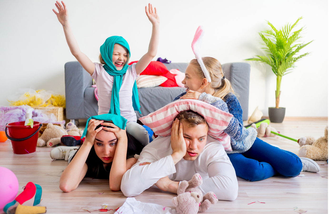 overwhelmed parents with happy kids with mess and toys behind them