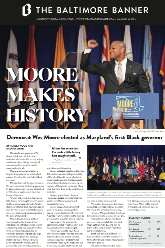 A man at a podium with a raised fist, smiling, at an event for the Maryland governor. Behind him are multiple flags and a large sign reading 'Moore Makes History'.