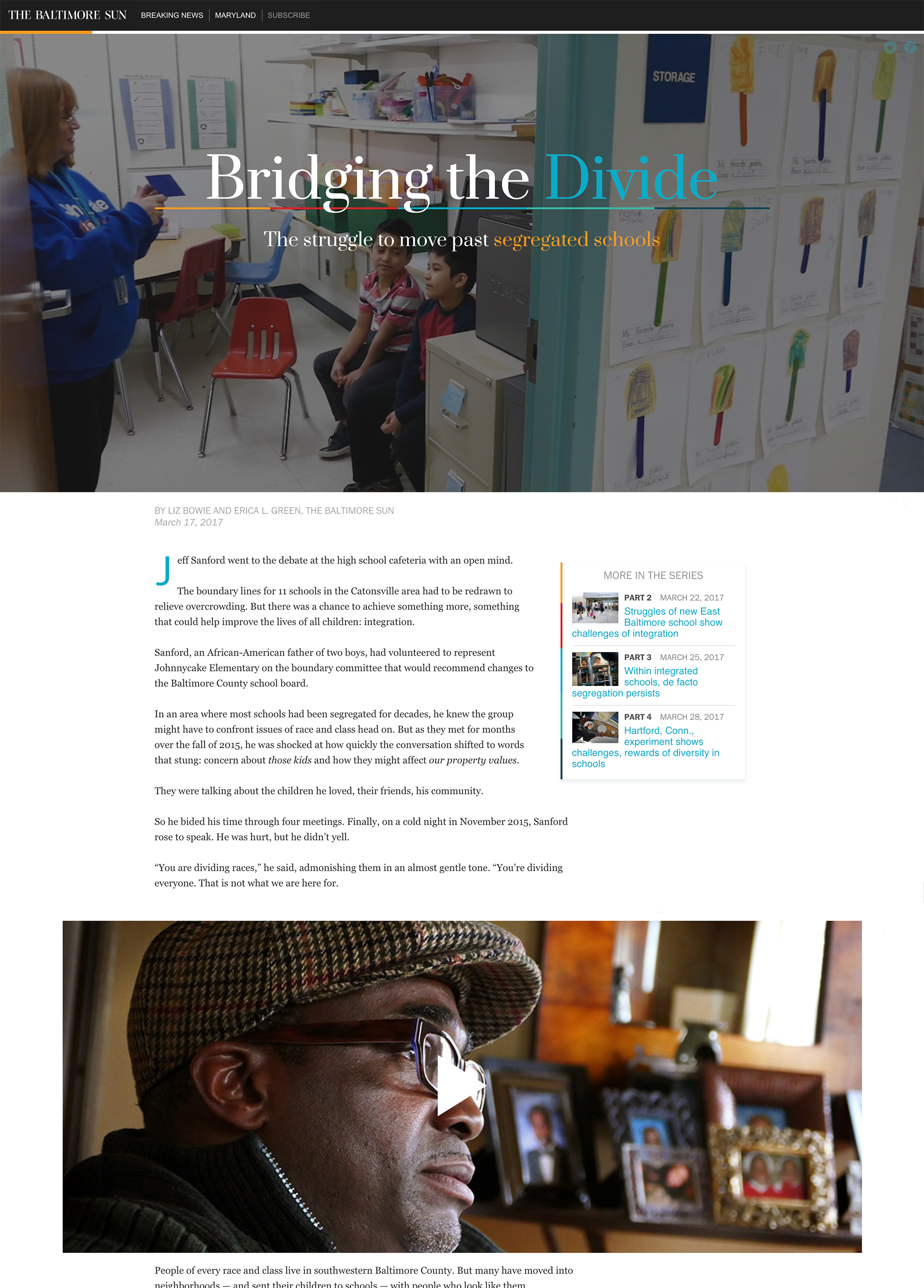 A woman with glasses wearing a plaid hat and a dark jacket, sitting indoors in front of a display of framed photographs and decorative items.