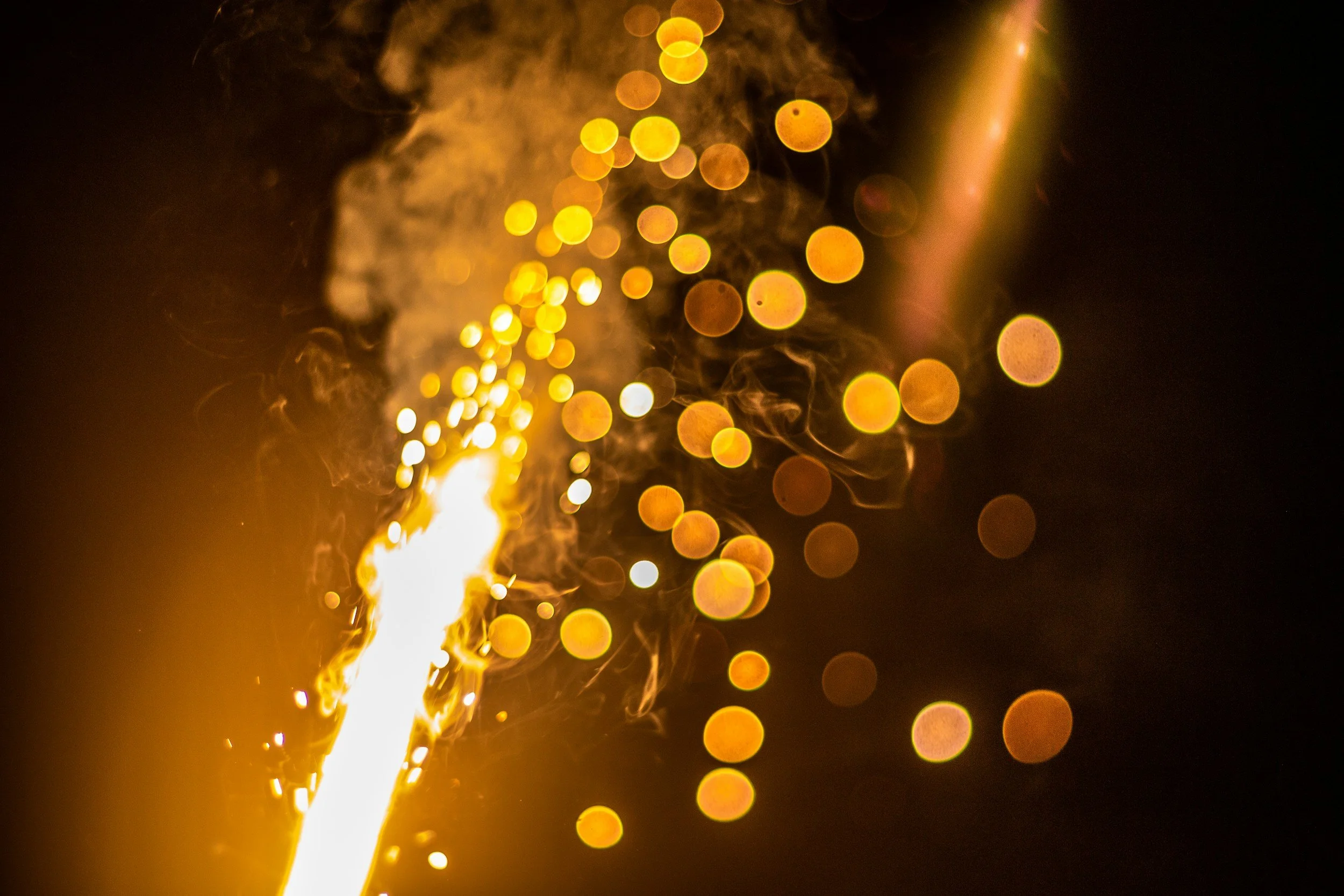 A bright sparkler with a trail of sparks and bokeh golden lights in the background.