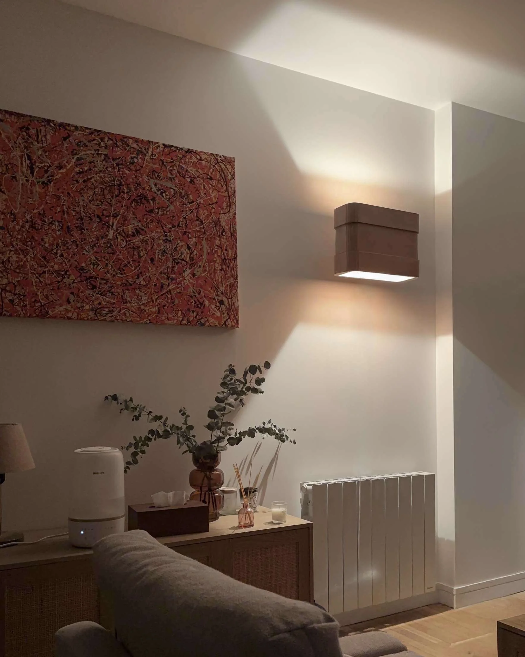 Salon intérieur avec une table basse, des vases, une lampe de luminothérapie, une plante et un tableau abstrait sur le mur, éclairé par un éclairage tamisé.