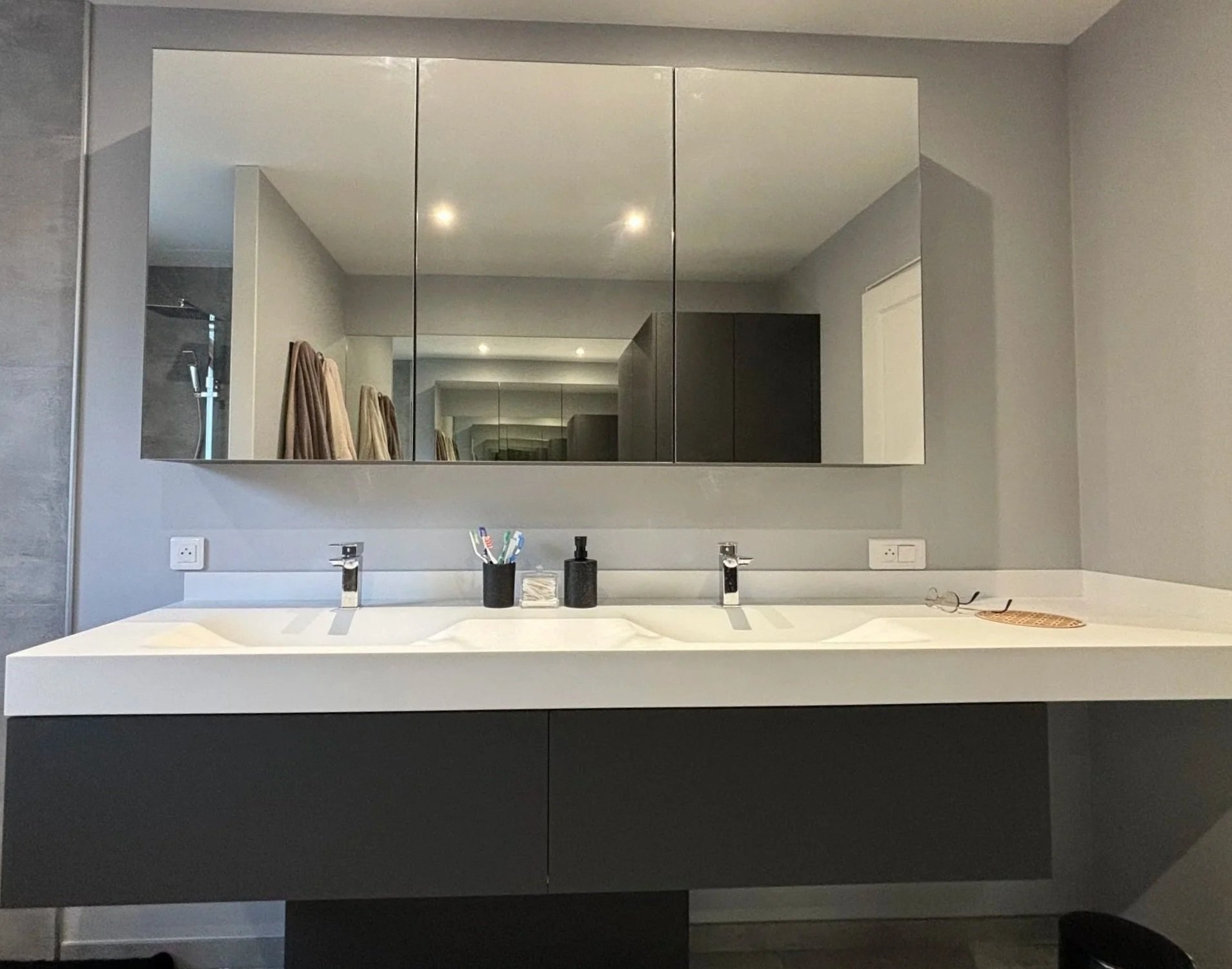 Un miroir au-dessus d'un lavabo blanc dans une salle de bain moderne. Deux distributeurs de savon.  Agencement sur mesure. Maison charnay.