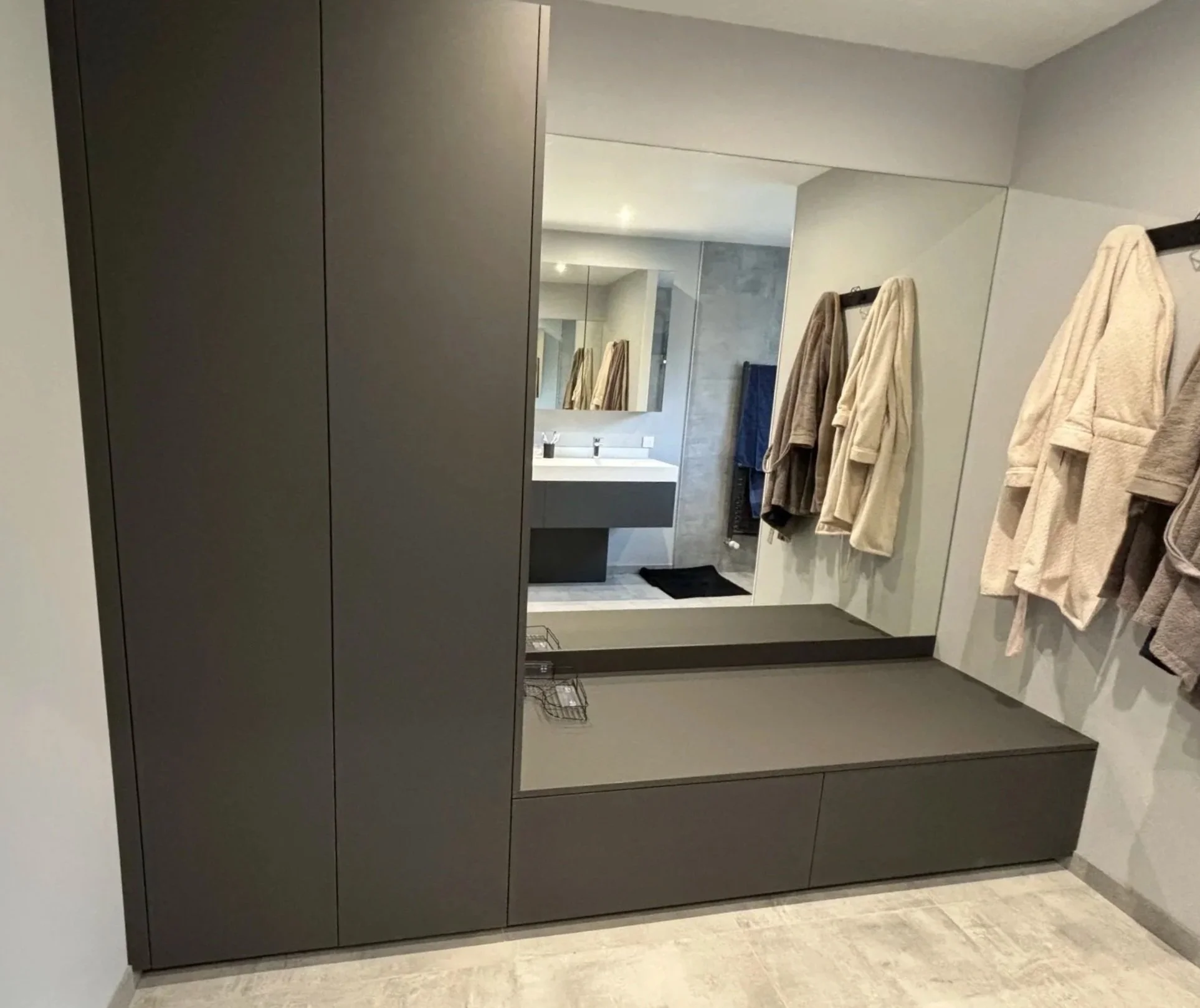 Miroir dans une salle de bain avec serviettes suspendues à un porte-serviettes et une armoire sombre.  Agencement sur mesure. Maison charnay.