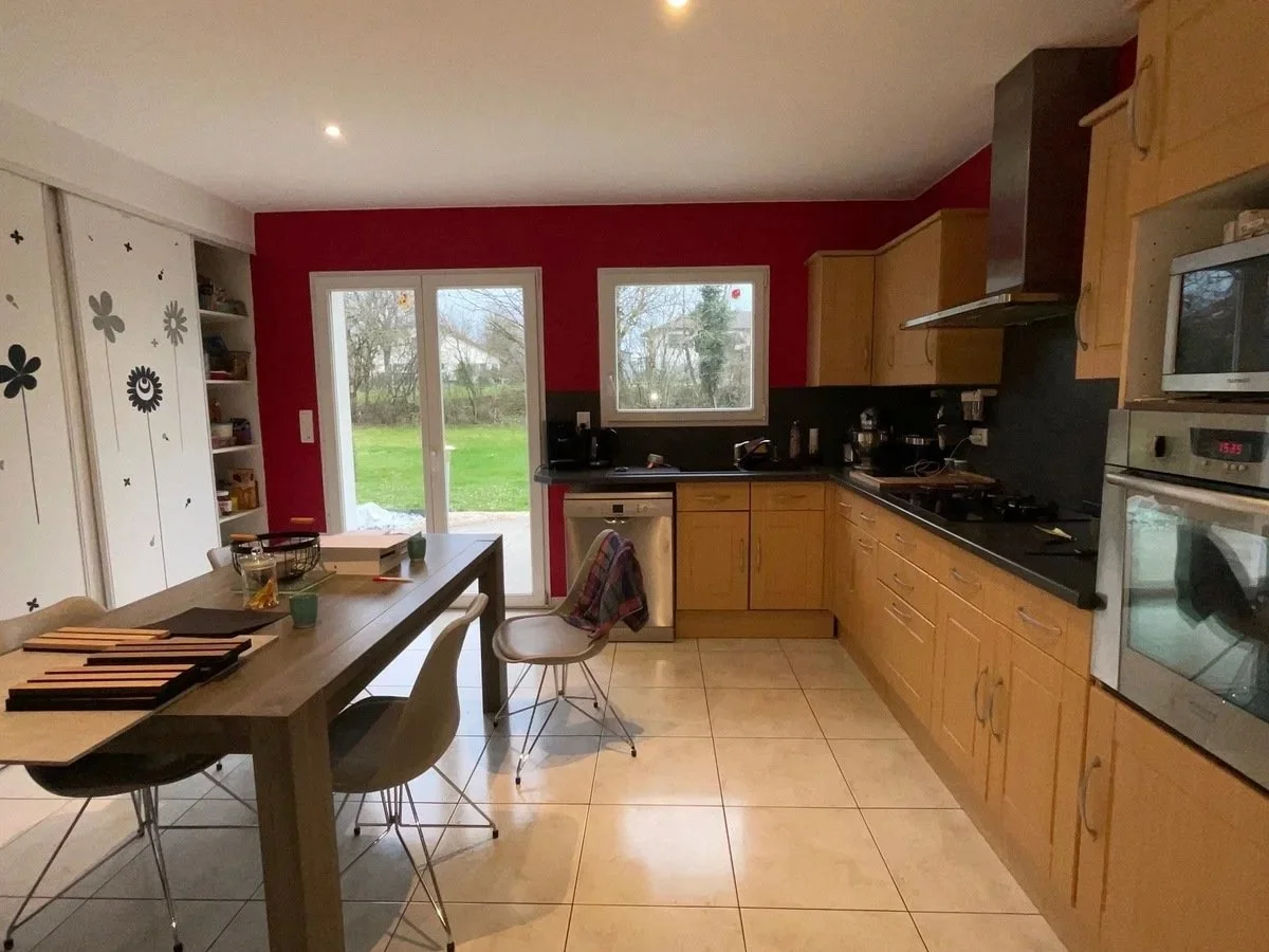 Cuisine existante de la maison rénovée à charnay avec murs rouges, armoires en bois, un plan de travail noir, deux fenêtres donnant sur un jardin et une porte-fenêtre.