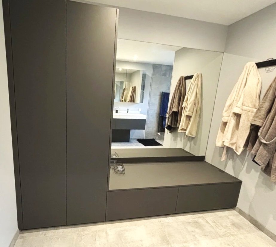 Miroir dans une salle de bain avec serviettes suspendues à un porte-serviettes et une armoire sombre.  Agencement sur mesure. Maison charnay.