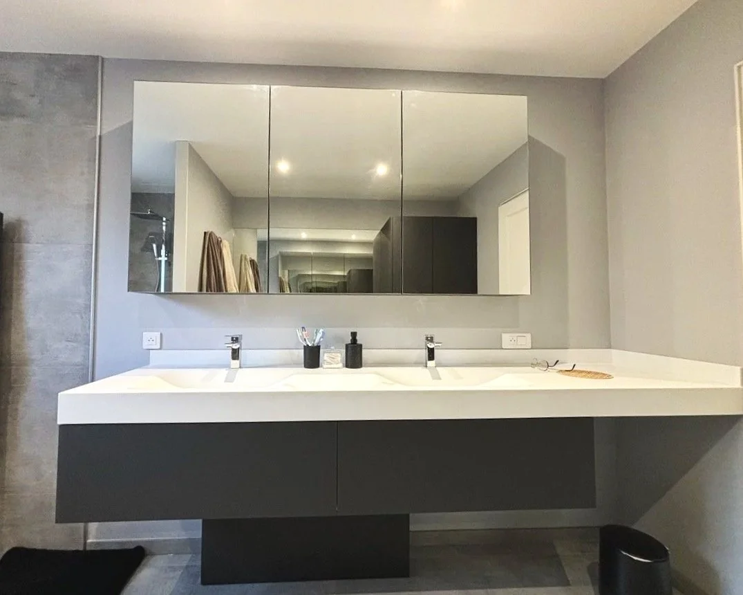 Un miroir au-dessus d'un lavabo blanc dans une salle de bain moderne. Deux distributeurs de savon.  Agencement sur mesure. Maison charnay.