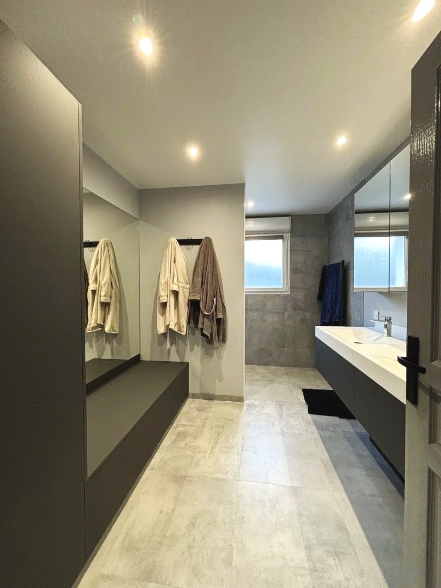 Salle de bain moderne avec baignoire, lavabo, miroir, fenêtre, et peignoirs suspendus. Agencement sur mesure. Maison charnay.