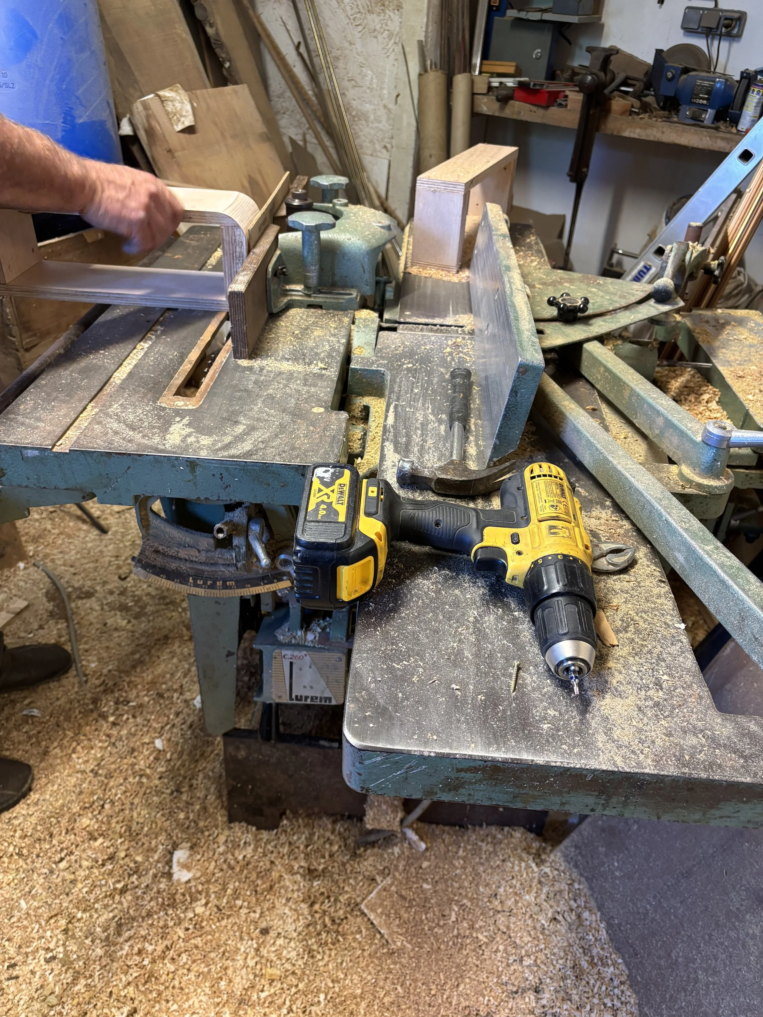 Un établi de bricolage avec une scie à onglet, une perceuse électrique et des morceaux de bois et de métal, dans un atelier de menuiserie ou de métallurgie.