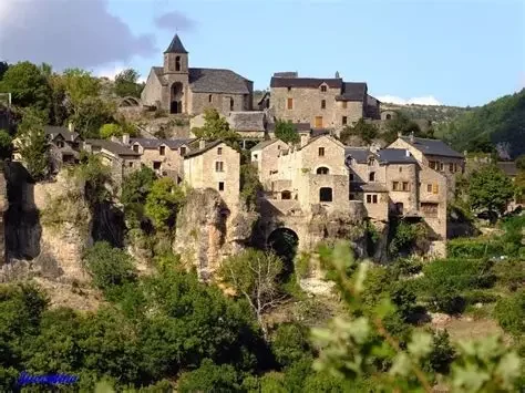 Village médiéval Cantobre dans l'Aveyron en pierre sur une colline avec une église et des maisons entourées de végétation.