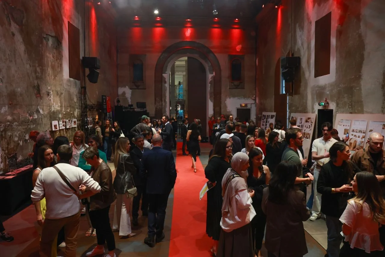 Une foule de personnes dans une galerie d'art ou un espace d'exposition, avec des murs abîmés en arrière-plan et un tapis rouge au sol.