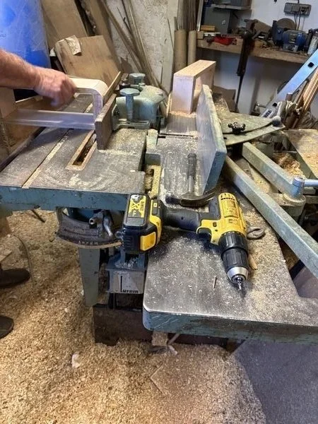 Conception de la maquette de l'applique (chambre d'hôtel 4*) pour le concours Talents d'archi 2025 Ynov x Formica dans un établi de menuiserie avec une scie à bande, une perceuse sans fil, et un niveau, dans un atelier de menuiserie.