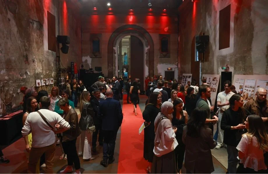 Une foule de personnes dans une galerie d'art ou un espace d'exposition, avec des murs abîmés en arrière-plan et un tapis rouge au sol.