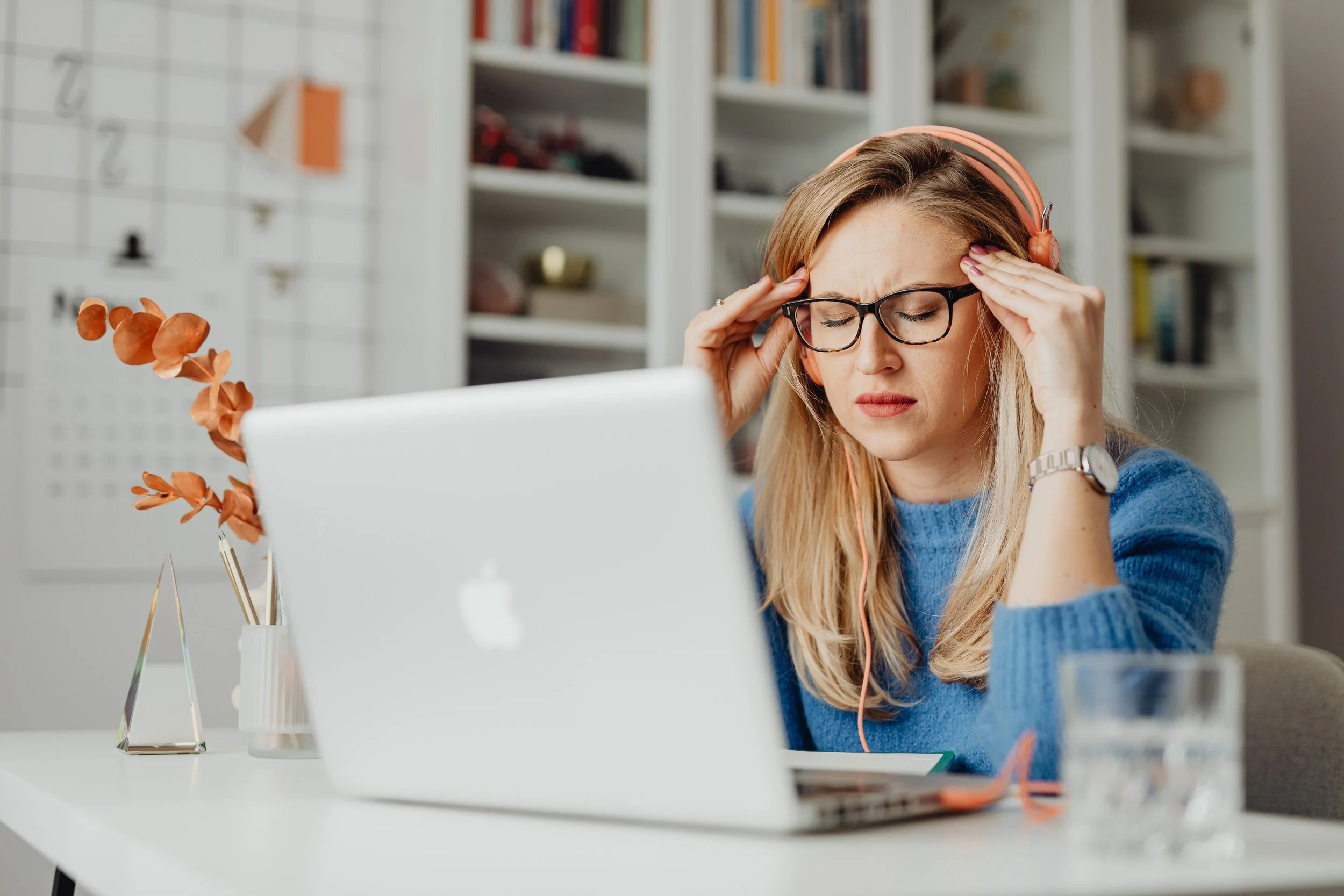 A tense woman rubbing her temples while working at a laptop