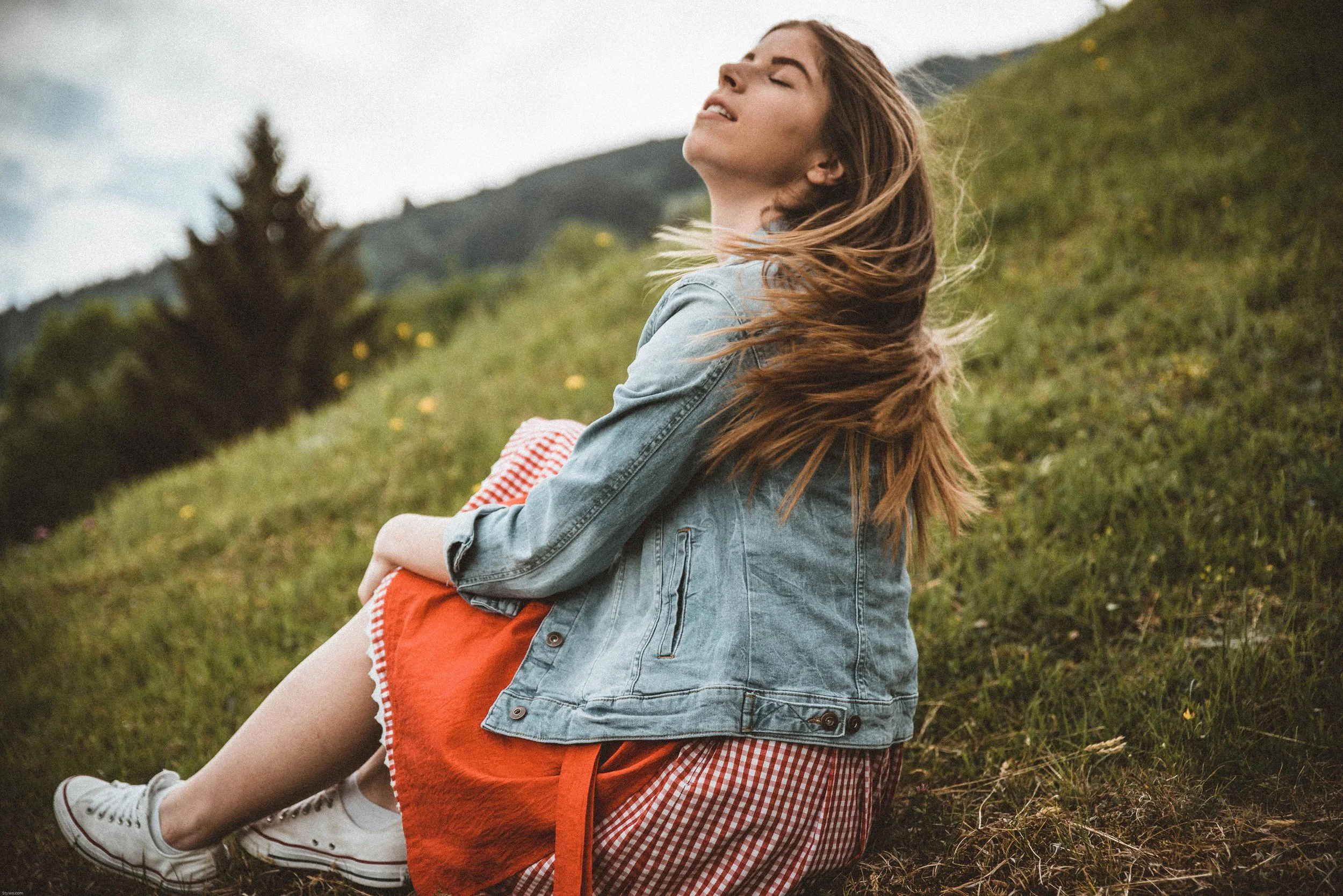 A woman sitting peacefully outdoors with her eyes closed, taking a deep breath