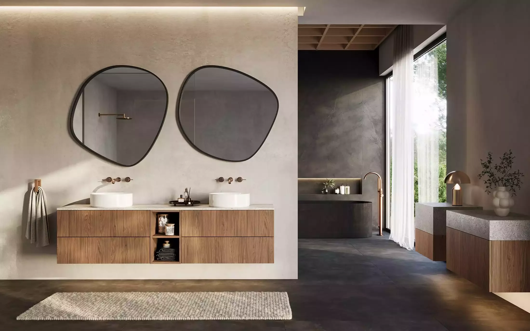 Modern bathroom with dual sinks on a wooden vanity, large oval mirrors, and a view of a shower with a dark wall and minimal decor, illuminated by natural light through a window.