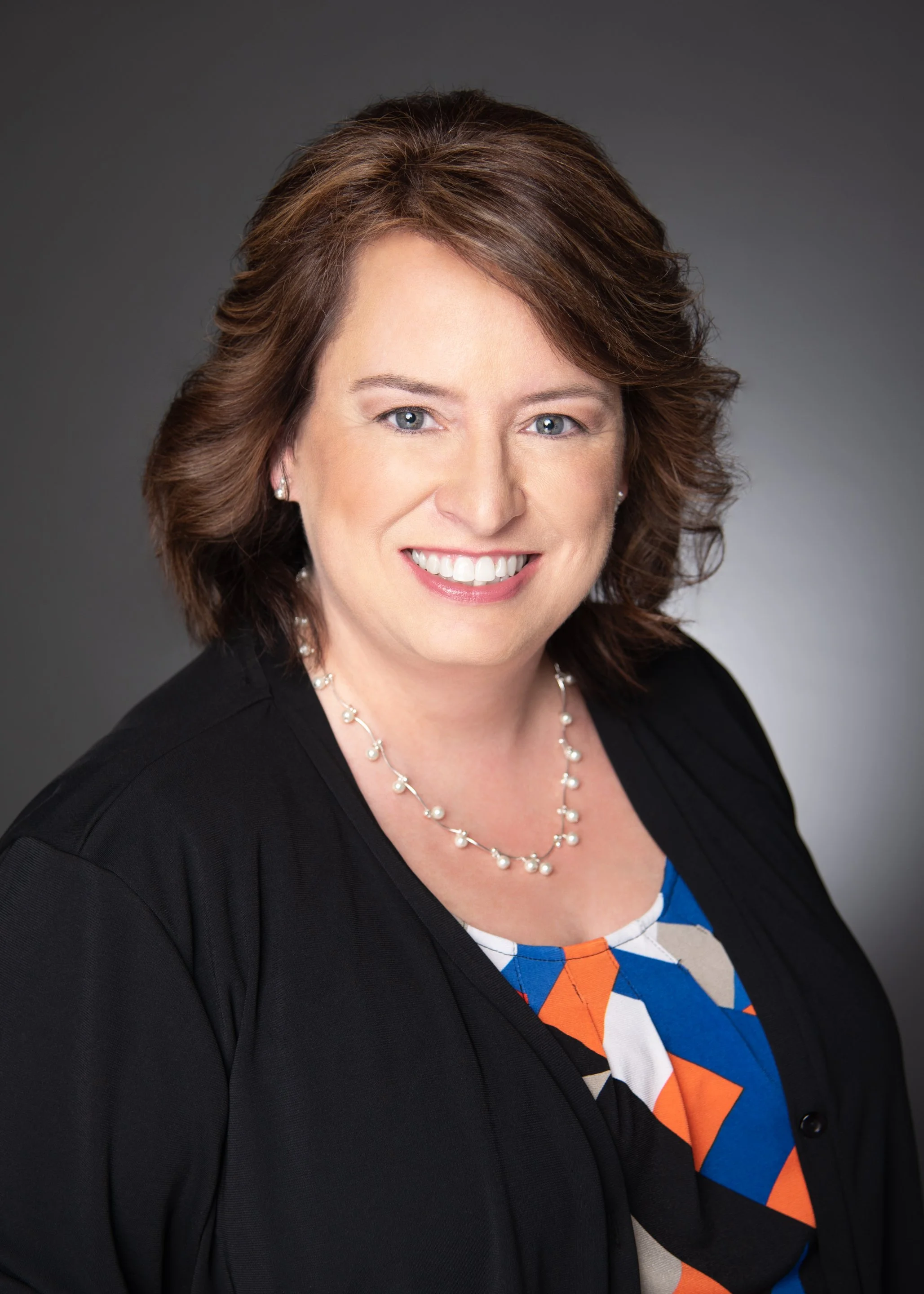 Professional headshot of Stephanie D. Leoni, LPC, with a warm, welcoming smile. She has dark shoulder-length curly hair and is wearing a black cardigan and pearl necklace.