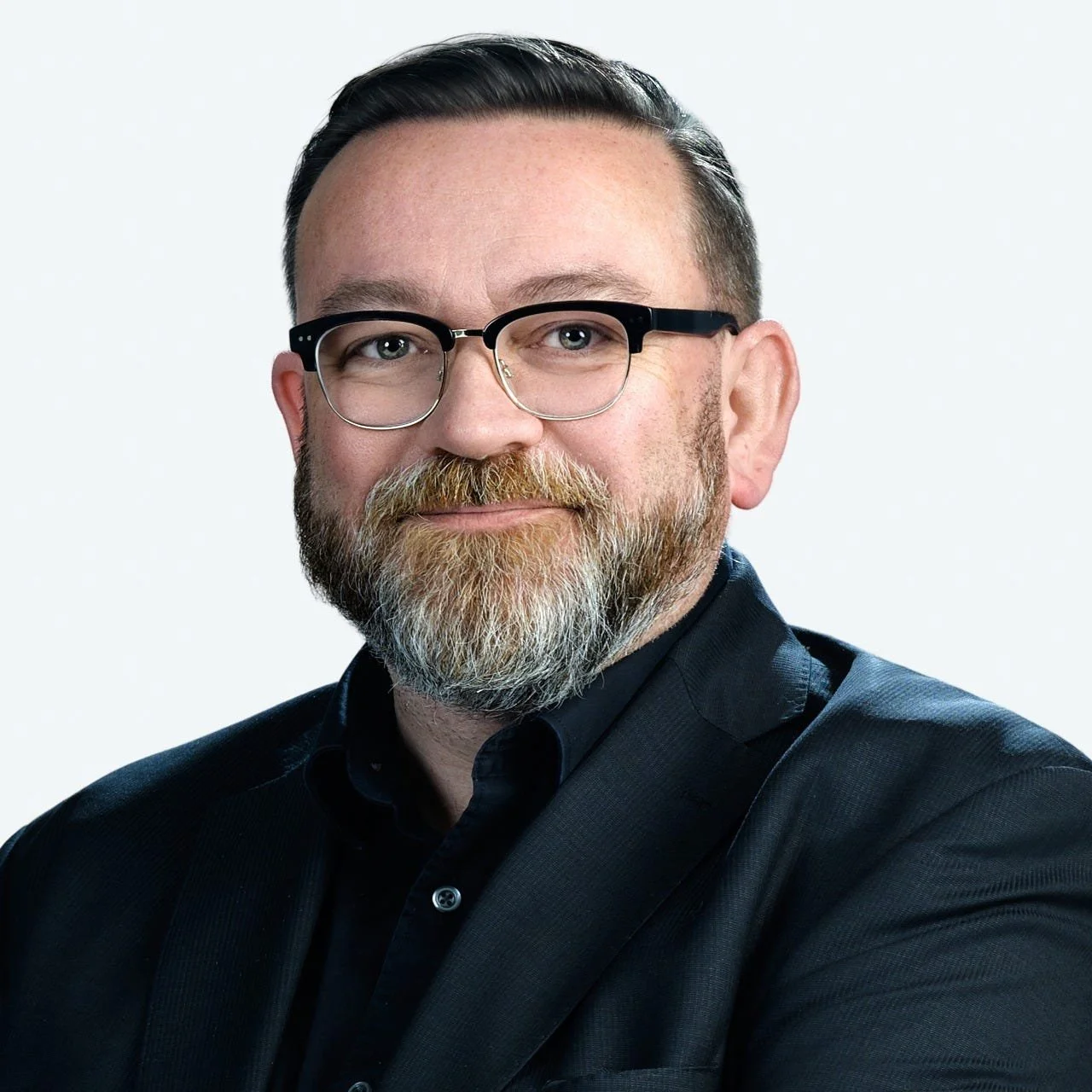 Headshot of a man with short dark hair, glasses, and a beard, wearing a dark shirt, against a plain white background.