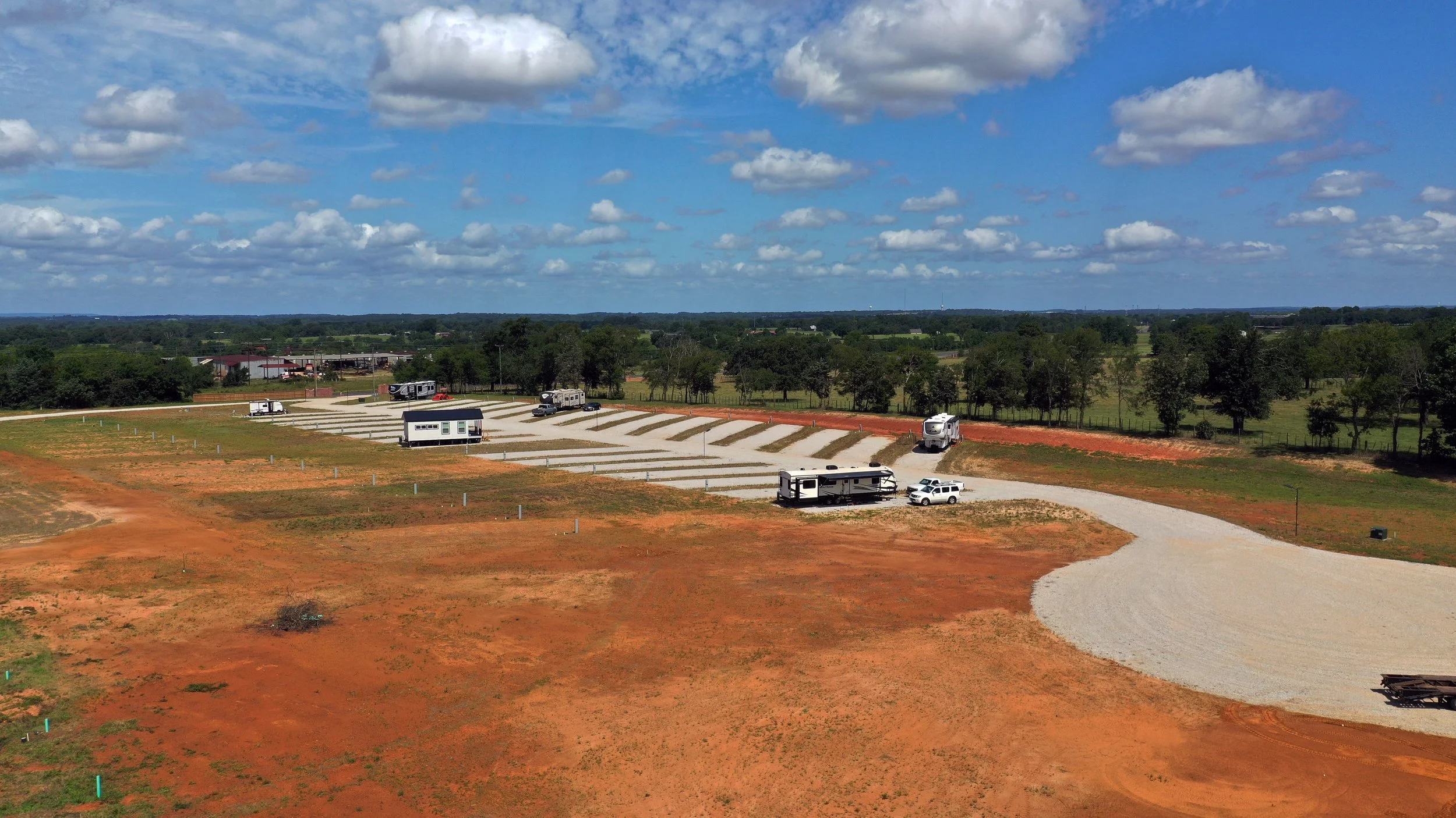 A landscape with a large sky filled with clouds and a rural area with parked RVs, trailers, and a gravel road under construction.