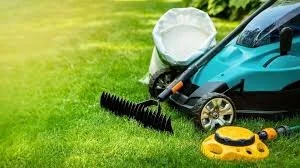 Lawn mower, leaf blower, and grass bag on a grassy lawn.